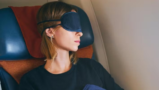 Woman with a sleep mask sleeping on a flight highlighting the best ways to avoid jet lag and stay healthy for your next long-haul flight